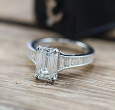 an emerald - cut diamond ring sits on a wooden surface