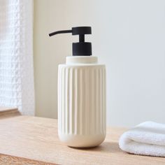 a white soap dispenser sitting on top of a wooden table next to a towel