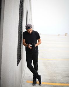 a man leaning up against a wall with a camera in his hand and looking down at the ground