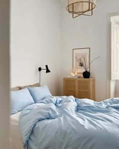 an unmade bed with blue sheets and pillows in a white room next to a window