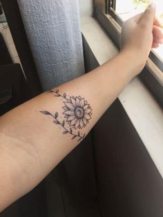 a person with a sunflower tattoo on their arm next to a window sill