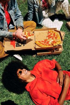 a woman laying on the grass with pizza in her hand and other people sitting around