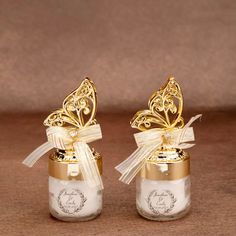 two glass jars with gold and white designs on them, one has a bow at the top