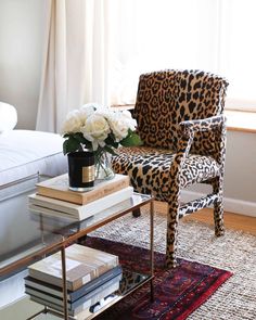 a leopard print chair in front of a window with white roses and books on it