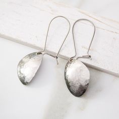 Simple and striking, these abstract titanium dangle earrings are sure to be a timeless favorite. Crafted from pure grade 1 titanium, these earrings are nickel-free and hypoallergenic, making them gentle on even the most sensitive ears. The lightweight and comfortable design is complemented by a subtle hammered silver texture, which creates an elegant surface that shines brilliantly in the light. Custom-made latching kidney wire hooks ensure a secure fit. Because these earrings are handmade, ther Modern Hammered Linear Earrings As Gift, Modern Teardrop Linear Earrings For Gift, Modern Teardrop Linear Earrings As Gift, Modern Hand Forged Earrings For Gift, Handmade Modern Teardrop Earrings, Modern Handmade Stainless Steel Earrings, Minimalist Metal Teardrop Earrings As Gift, Modern Hammered Linear Earrings For Gift, Modern Metal Hypoallergenic Teardrop Earrings