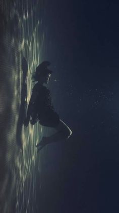 a woman standing in the water with her legs spread out and head down, looking up