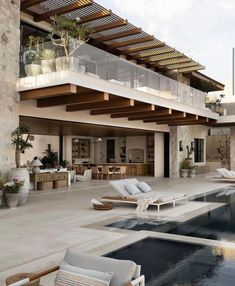 an outdoor swimming pool with lounge chairs and potted plants next to it in front of a house