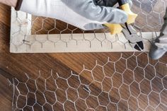 a person with a pair of pliers cutting through chicken wire on a wood floor