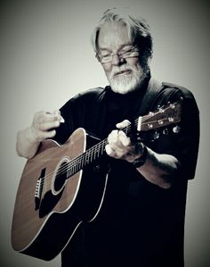 a man with glasses playing an acoustic guitar