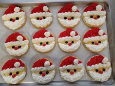 twelve decorated cookies in the shape of santa claus's head on a baking sheet