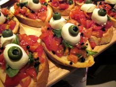 several appetizers with olives, tomatoes and other toppings are arranged on a cutting board