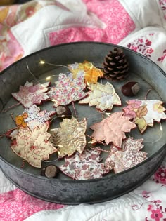 a metal bowl filled with lots of different types of autumn leaves on top of a quilt