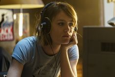 a young woman wearing headphones sitting in front of a computer monitor and looking at the screen