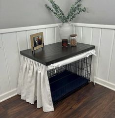 a table with a dog crate underneath it on top of a hard wood floor next to a plant