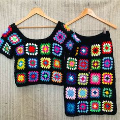 two crocheted sweaters hanging on a wooden hanger next to each other