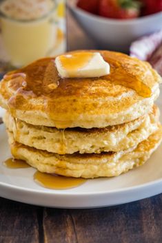 a stack of pancakes with butter and syrup on a plate next to a bowl of strawberries