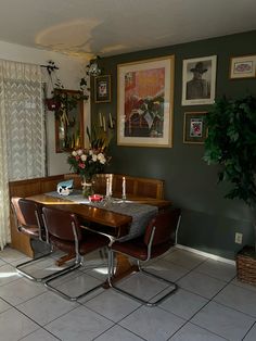 a dining room table and chairs with pictures on the wall behind them, in front of a potted plant