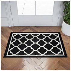 a black and white door mat on the floor next to a potted green plant