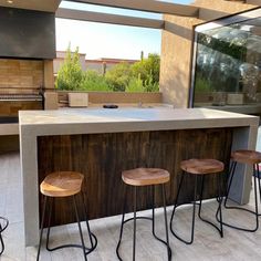 an outdoor kitchen with three stools next to the counter top and grill in the background