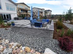 an outdoor patio area with rocks, gravel and blue chairs in the foreground on a sunny day