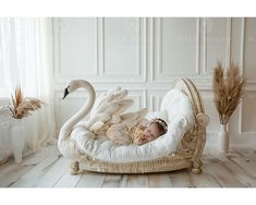 a baby sleeping in a swan shaped bed with feathers on the back and head resting on it