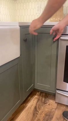 a person reaching for something on the counter in a kitchen with green cabinets and wood flooring