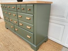 a green dresser with brass knobs on it's drawers next to a door