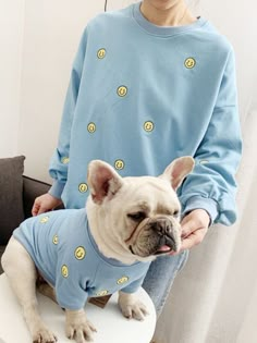 a woman sitting on top of a toilet with a small dog wearing a blue shirt