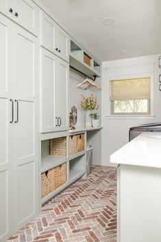 a kitchen with brick flooring and white cabinets in the center, along with baskets on the shelves