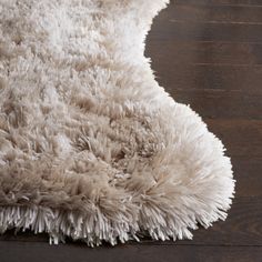 an area rug with white shag on top of wooden flooring and dark wood floors