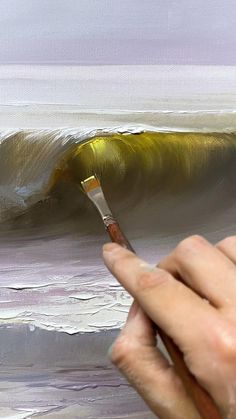 a person holding a paintbrush in front of an oil painting of a large wave