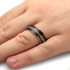 a person's hand with a black and gold wedding ring on their left hand