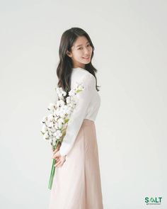 a woman in a white shirt and pink skirt holding a bouquet of flowers with her hands behind her back