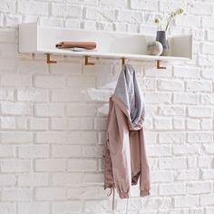 a white brick wall with two coats hanging from hooks and a vase on the shelf