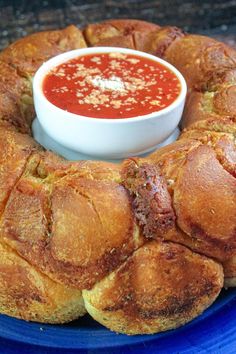 a blue plate topped with rolls covered in bread next to a bowl of tomato sauce