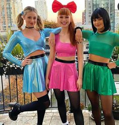 three young women in costumes posing for a photo on top of a building with their arms around each other