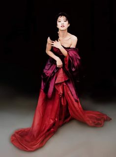 a woman in a red and purple dress with her hands on her chest, posing for the camera