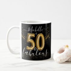 a black and gold 50th birthday mug next to a donut