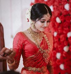 a woman in a red and gold sari smiles as she stands next to a flower arrangement