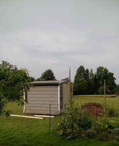 an outhouse in the middle of a field with trees and bushes around it on a cloudy day