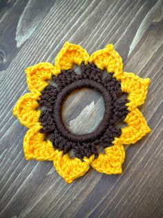 a crocheted yellow and brown sunflower on a wooden surface with a hole in the center