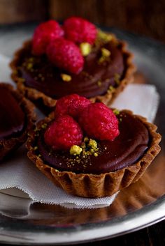 three chocolate tarts with raspberries and pistachio toppings on a plate