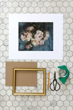 a painting and some scissors are sitting on the counter next to a framed photo with flowers in it