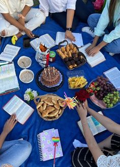 a group of people sitting around a blue table with food on it and open books