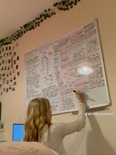 a woman writing on a white board in front of a wall covered with pictures and birds