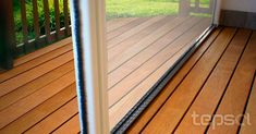 an open sliding glass door on a wooden deck with grass and trees in the background