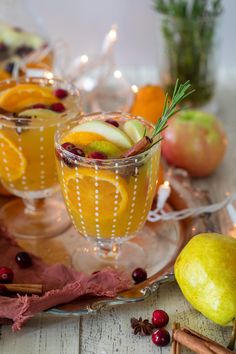 two glasses filled with oranges and cranberries on a plate next to apples