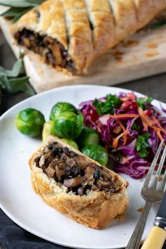 a white plate topped with meat and veggies next to a pastry on a cutting board