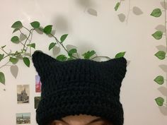 a woman wearing a black knitted cat hat with green leaves on the wall behind her