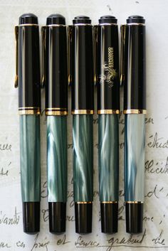 four fountain pens lined up on top of an old handwritten paper with writing in the background